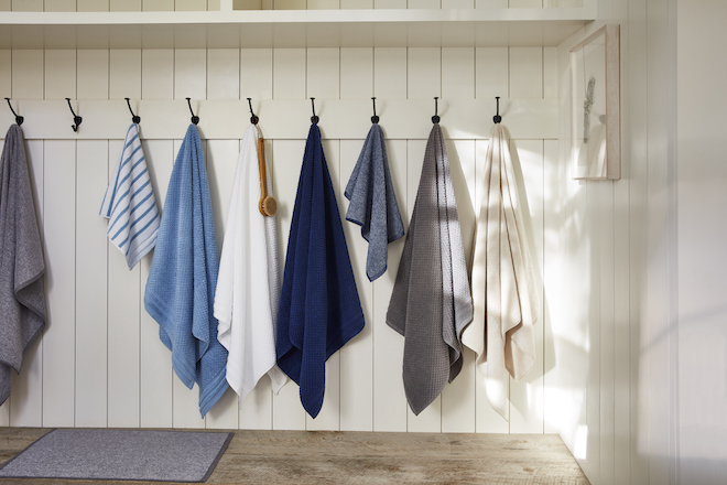 Bathroom towels in different patterns and shades hanging on wall hooks.