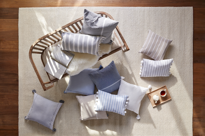 A pile of throw pillows in shades of blue, beige, and grey scattered on a beige rug.